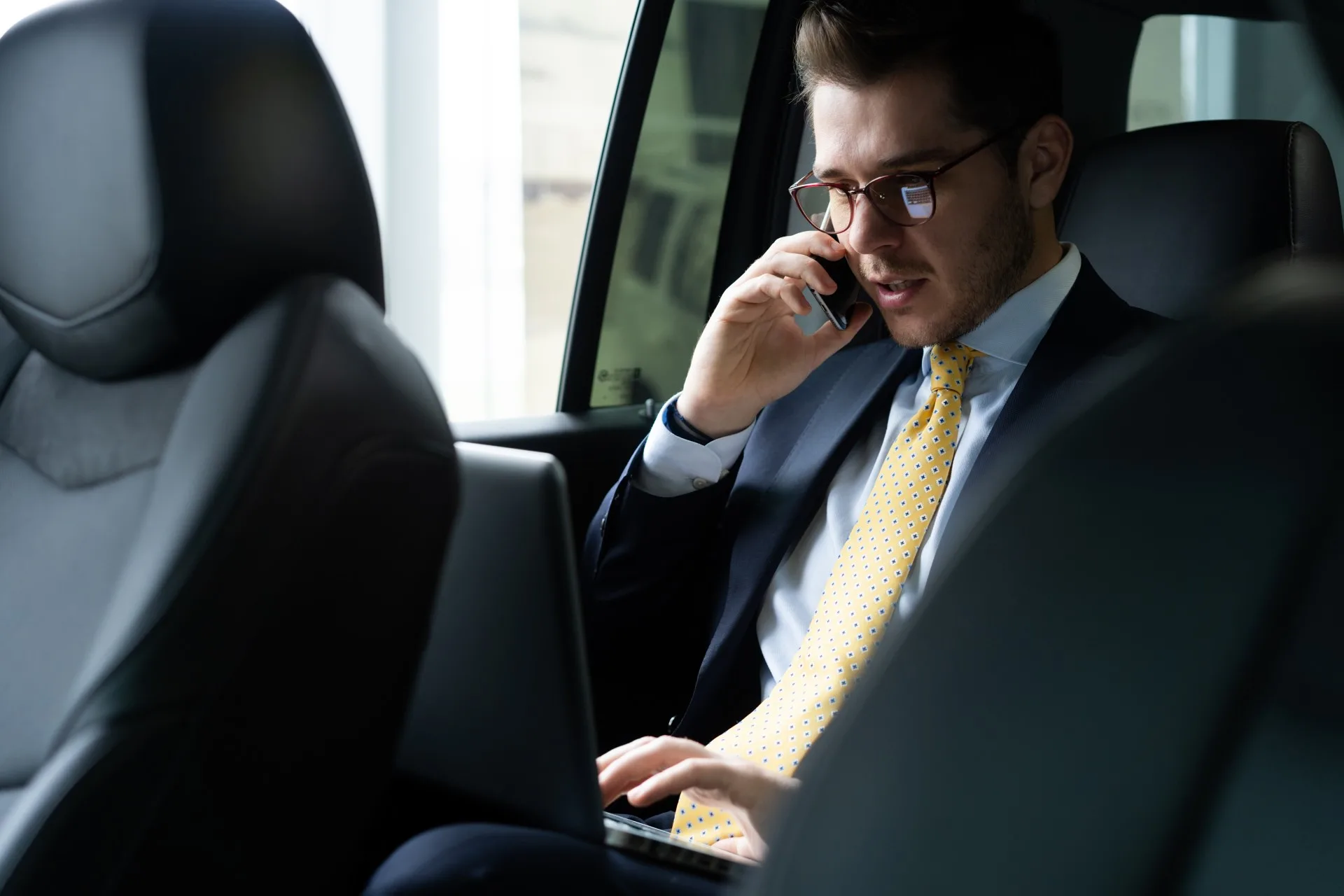 Young businessman sitting back seat car while his chauffeur is driving automobile